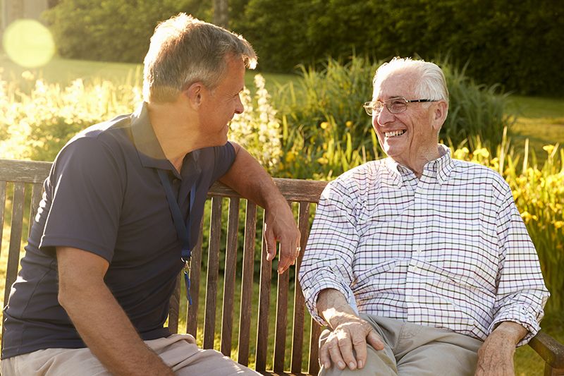 An elderly friend sitting on a bench and laughing together, representing respite care services in Allen, TX